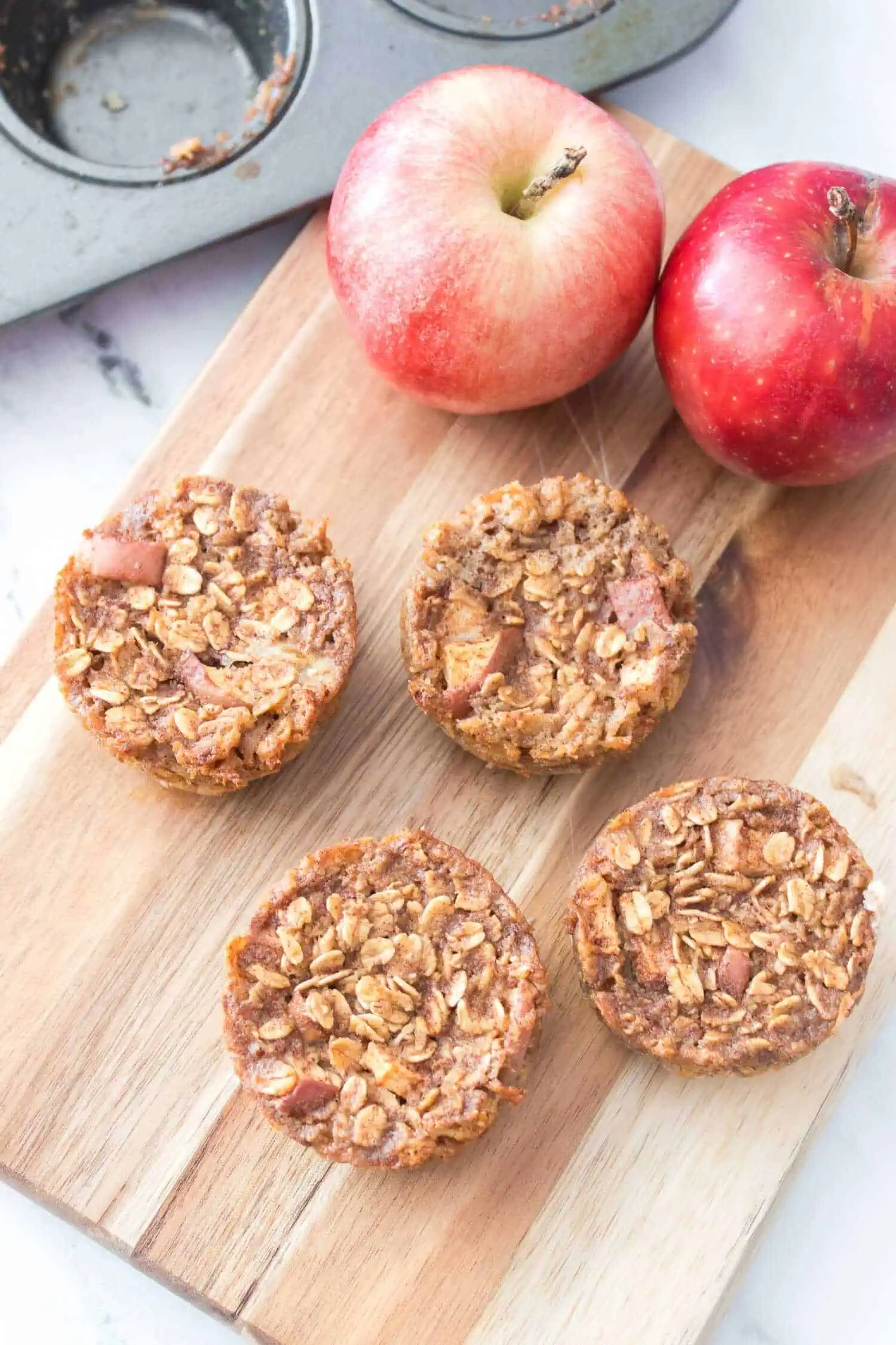 Apple cinnamon oatmeal cookies on a wooden board with two apples.