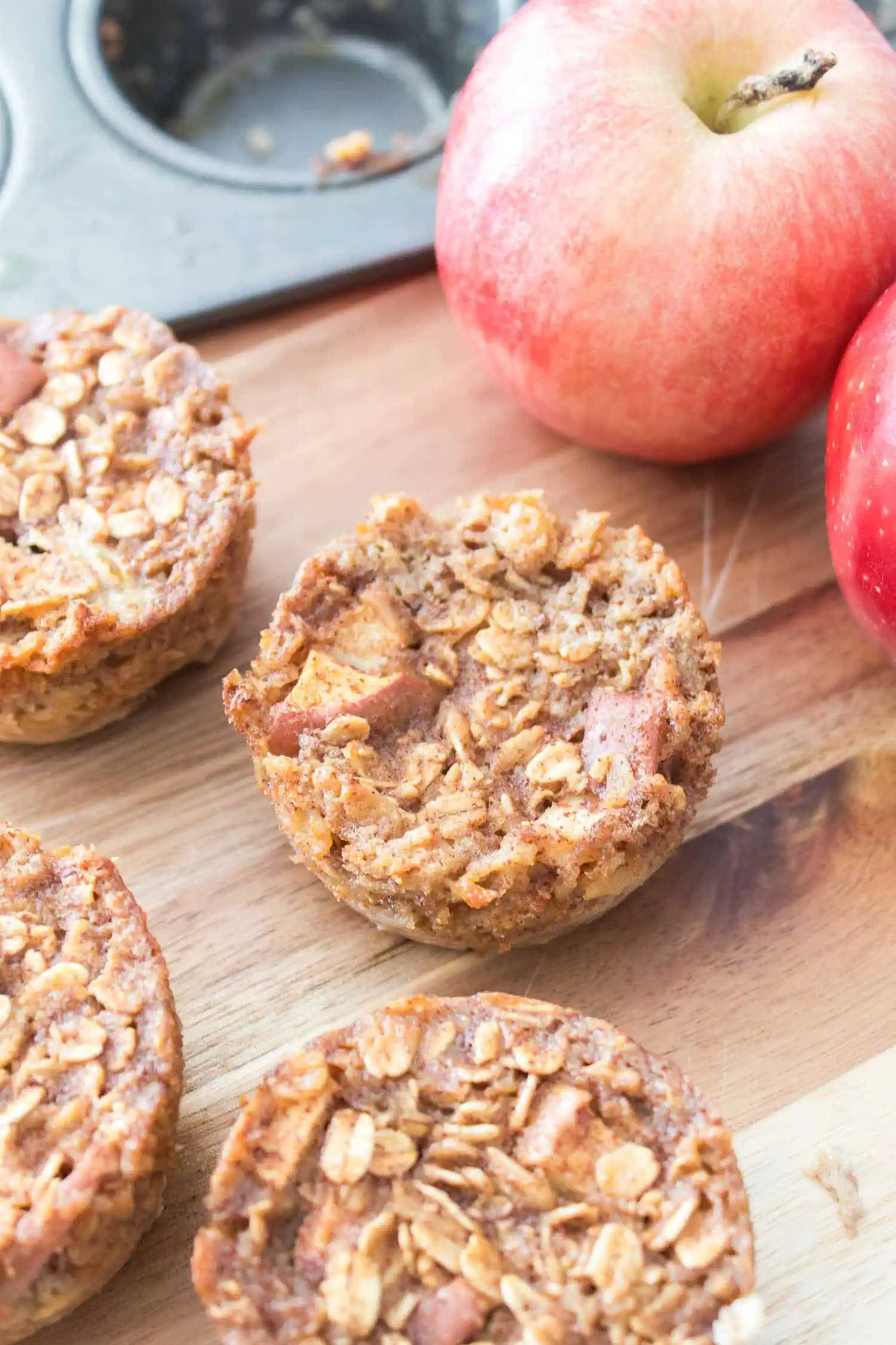 Delicious apple oatmeal muffins on wooden board with apples in background.