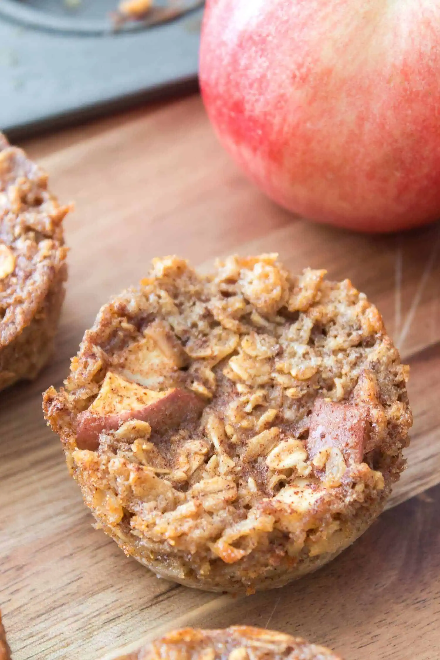 Oatmeal apple muffins on a wooden surface with a fresh apple in the background.