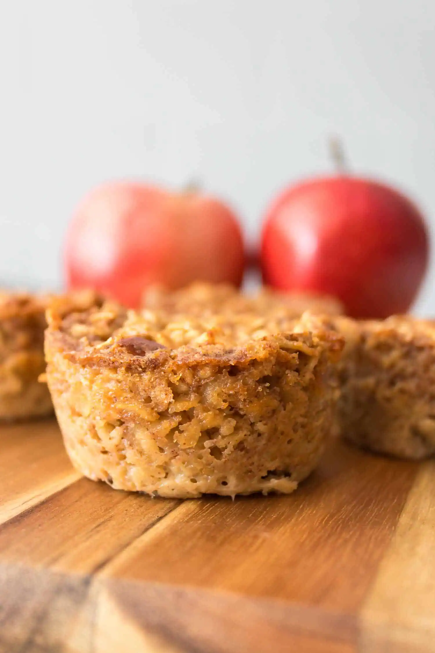 Golden apple cinnamon oatmeal muffins with fresh apples on a wooden surface.