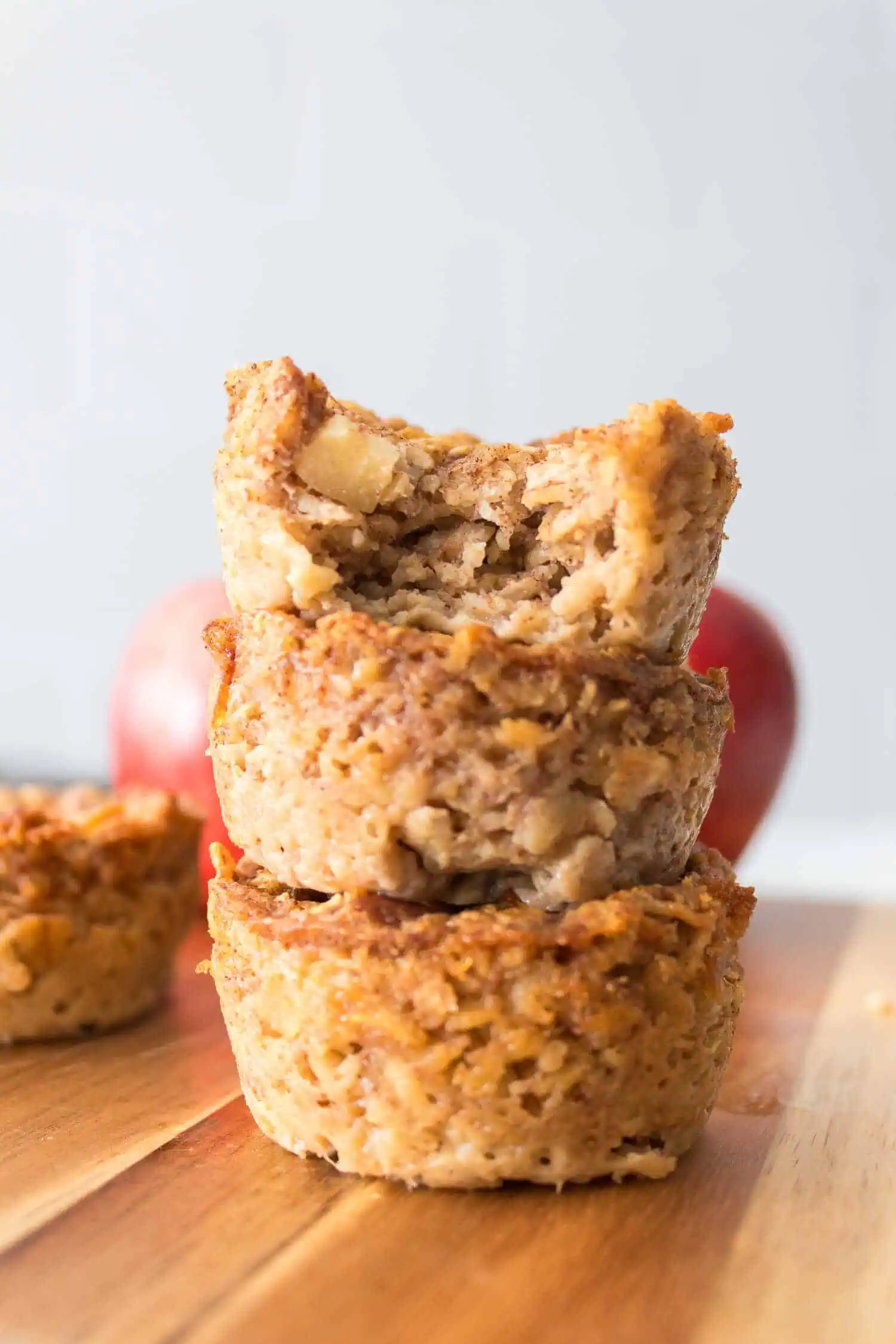Golden oatmeal cookie with apple chunks stacked on a wooden surface with fresh apples in the background, healthy baking, homemade snacks, healthy dessert.