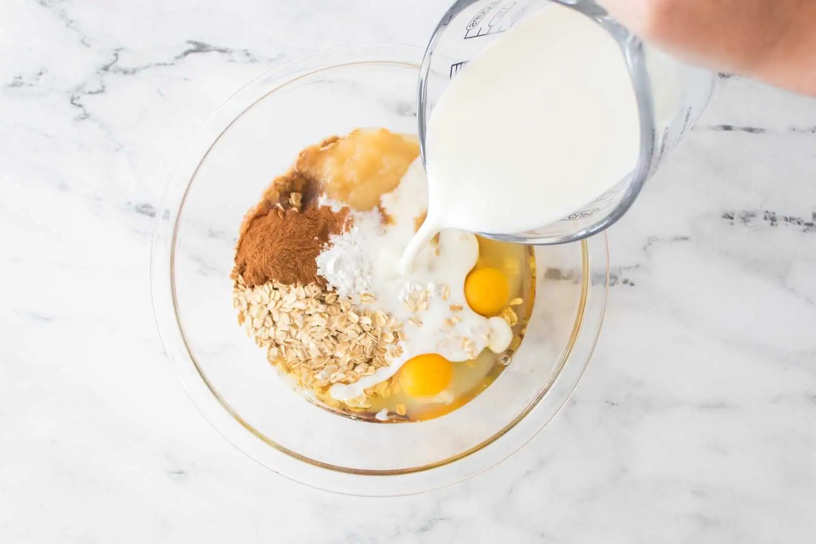 Cream being poured into a bowl of oats, eggs, and spices for baking or cooking.