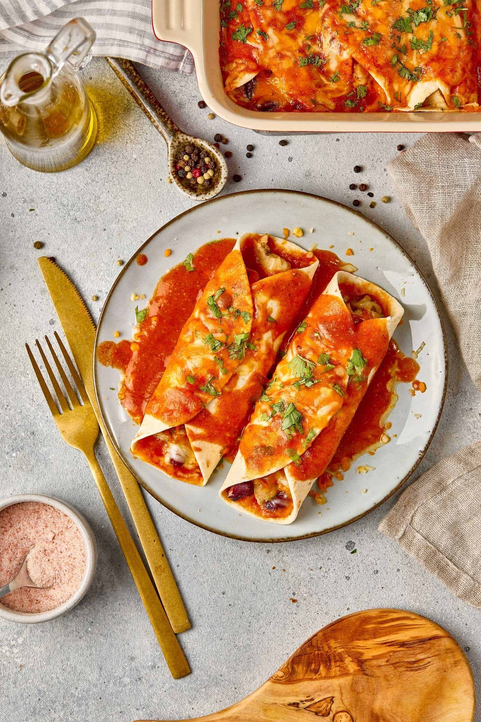 Delicious beef burritos topped with melted cheese, fresh herbs, and savory sauce on a white plate.