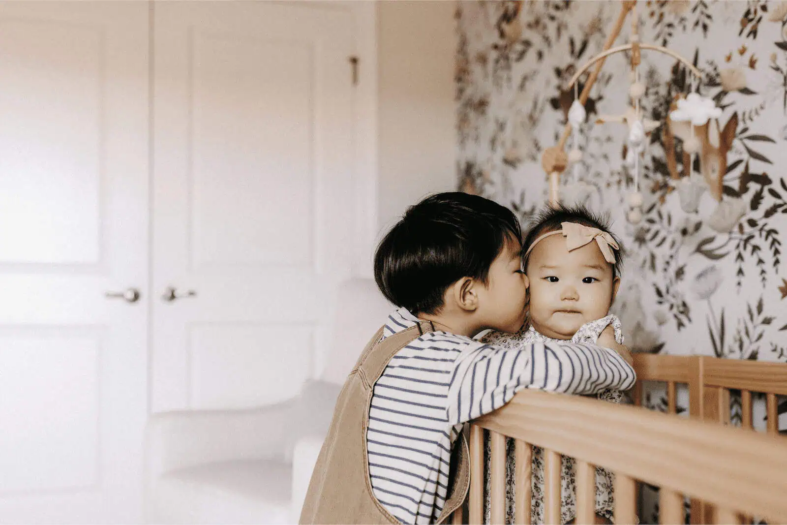 Sweet Asian siblings sharing a tender moment in the nursery, showcasing surrogate family love and bonding.