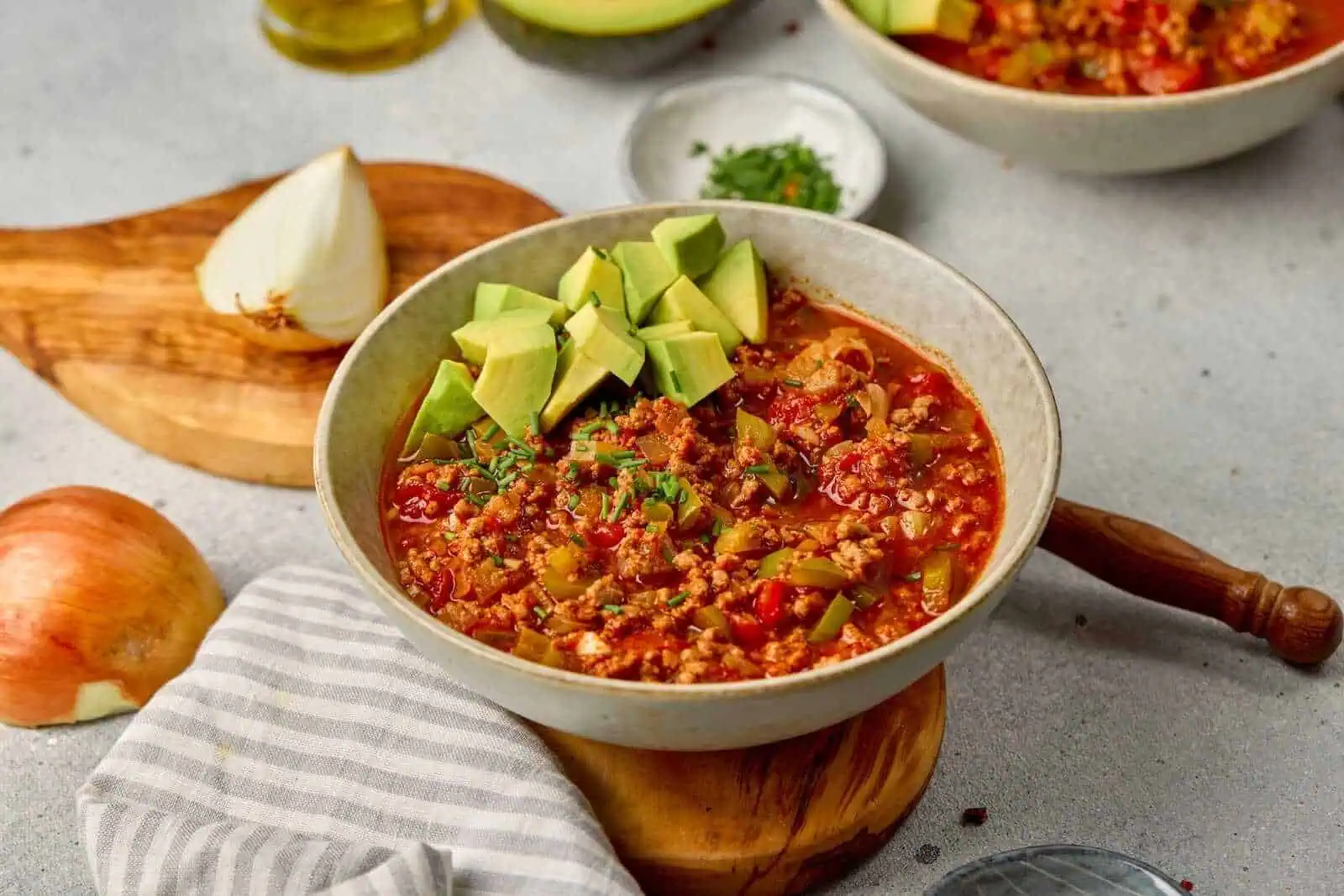 Savory taco soup with avocado and ground meat in a ceramic bowl on gray surface.
