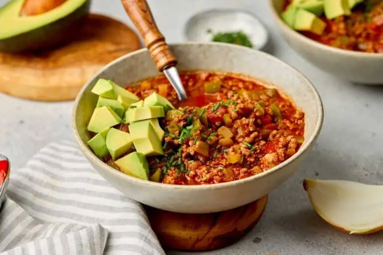 Creamy tomato-based chili with avocado and herbs in a rustic bowl.