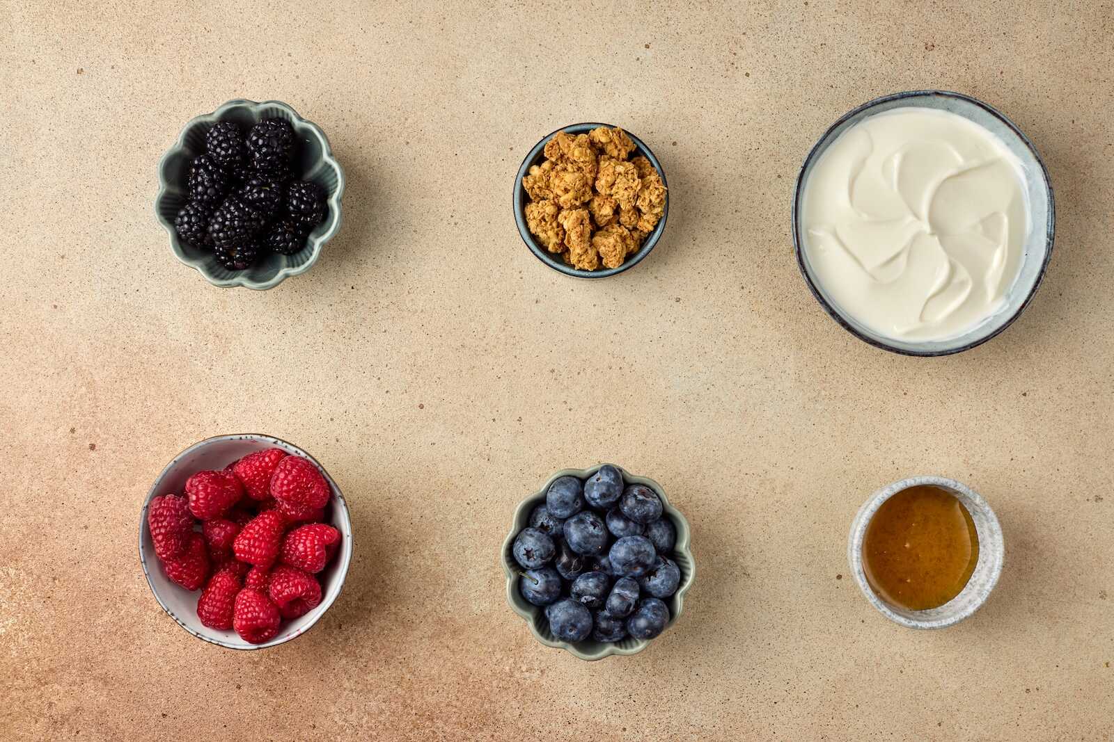 Fresh mixed berries, yogurt, granola, and honey on a neutral background.