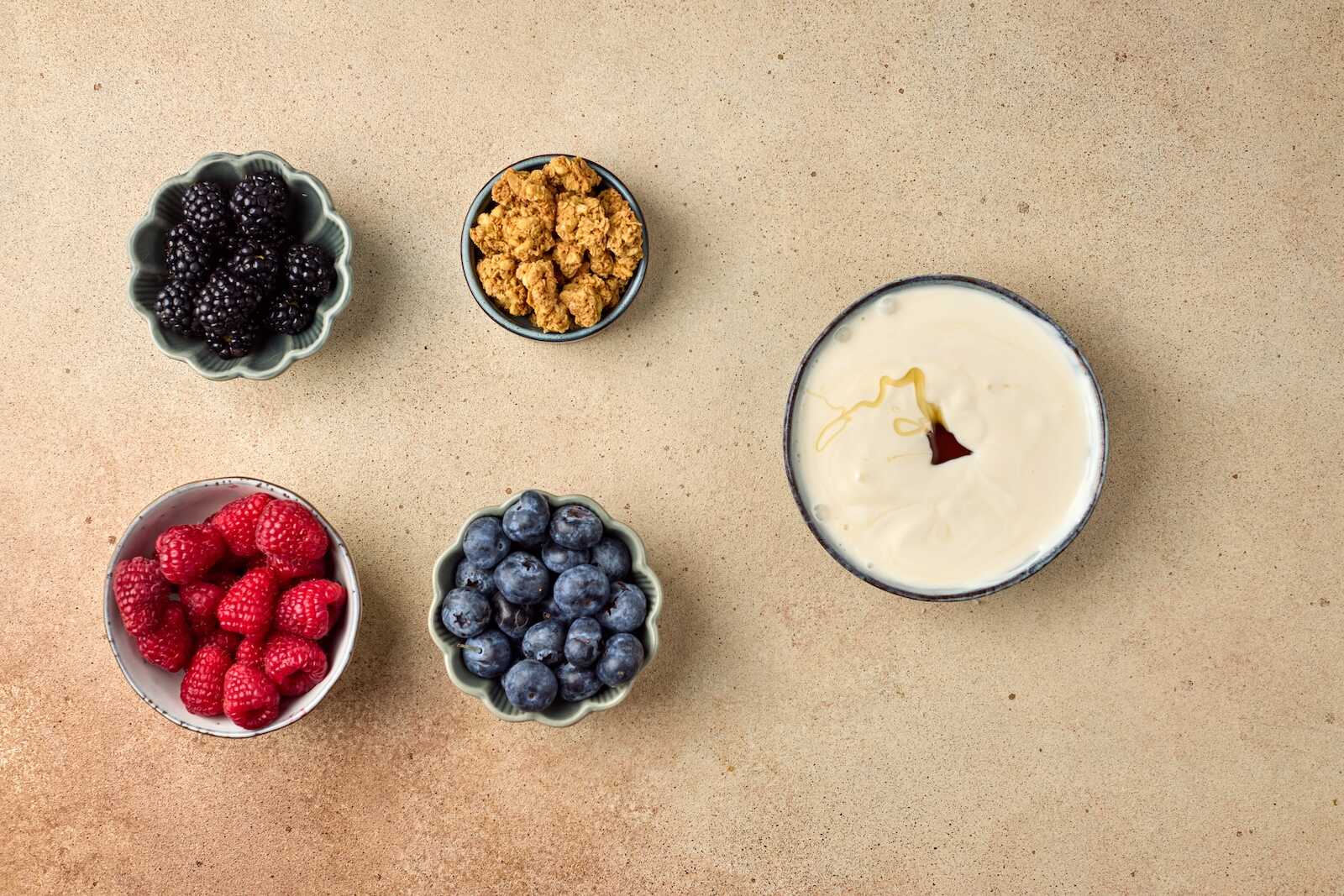 Fresh blackberries, raspberries, blueberries, granola, and honey yogurt parfait on a beige surface for a nutritious snack.