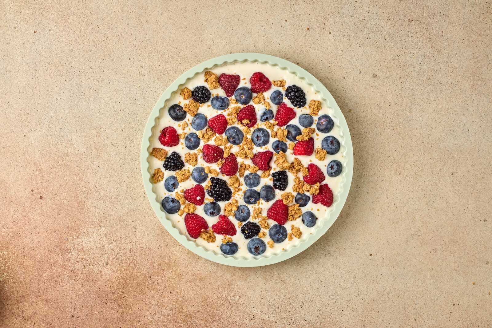 Colorful mixed berry yogurt tart with granola topping on a neutral background.