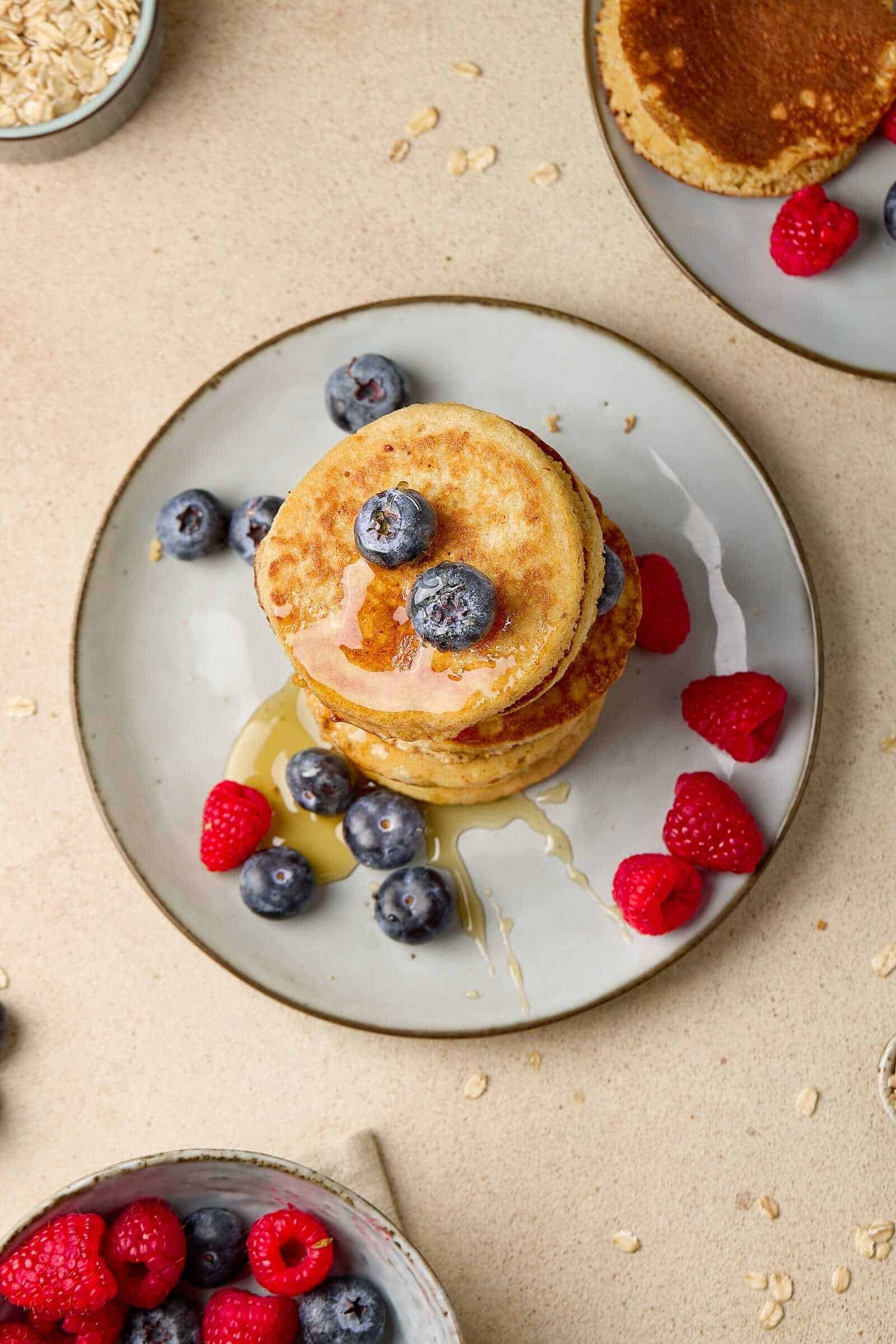 Delicious pancakes topped with blueberries, raspberries, honey, and syrup on a plate.