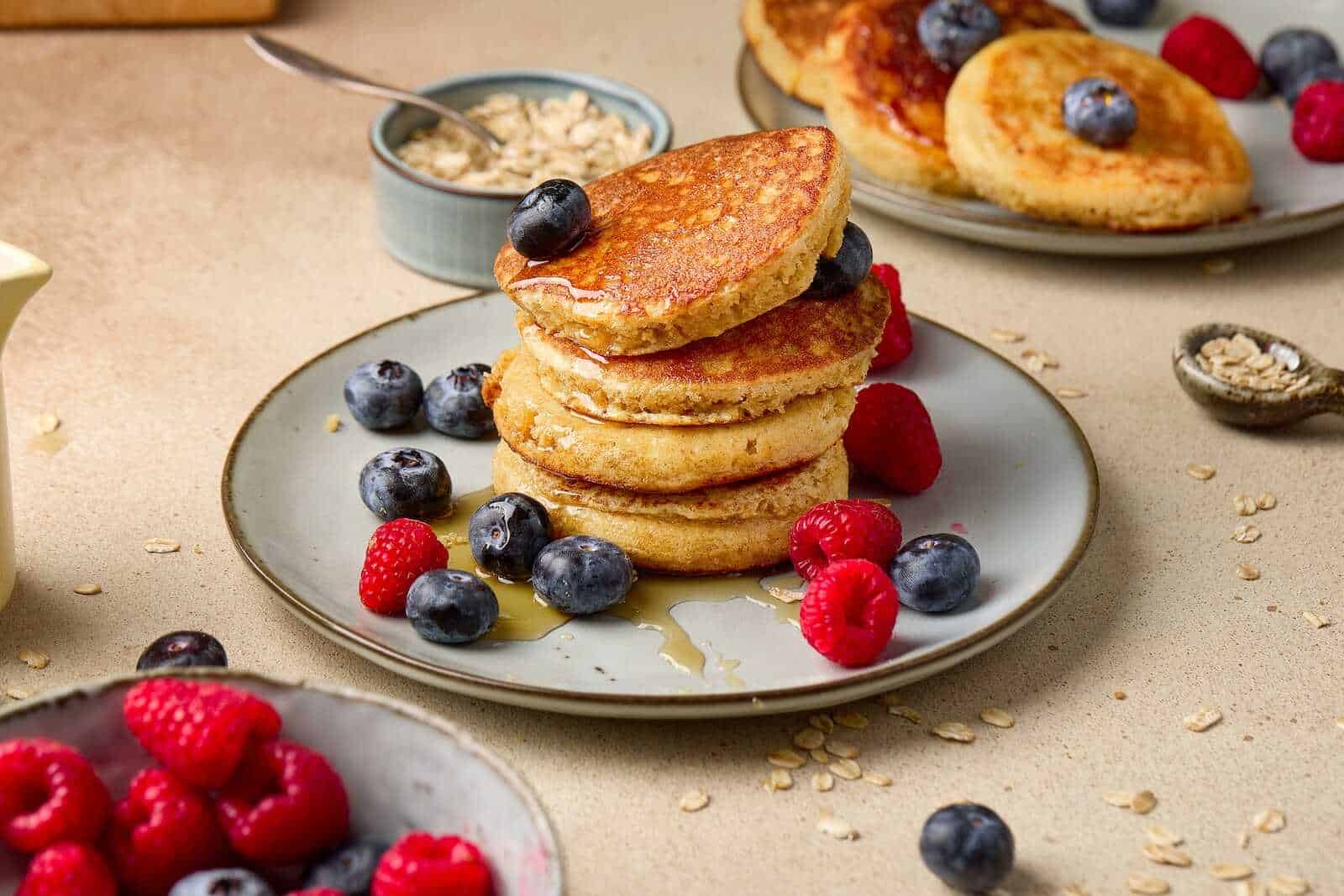 Delicious stack of blueberry and raspberry pancakes drizzled with syrup, served with fresh berries and oats.