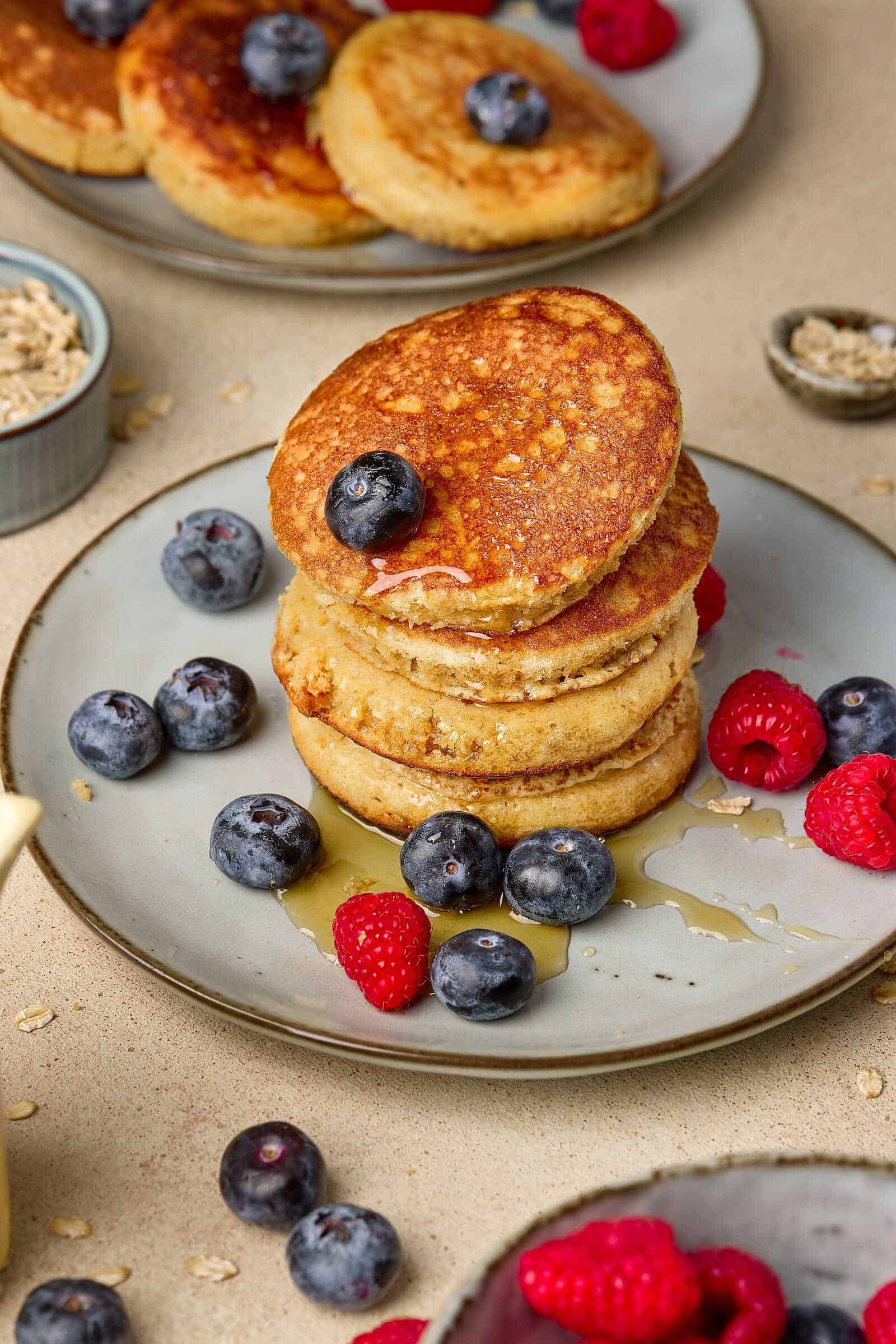 Delicious golden-brown pancakes topped with blueberries and raspberries, drizzled with honey for a nutritious breakfast.