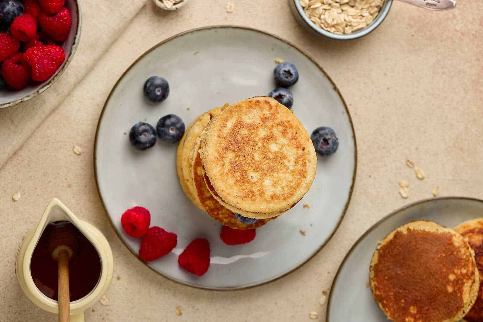 Delicious homemade blueberry and raspberry pancakes served with honey, fresh berries, and oatmeal.