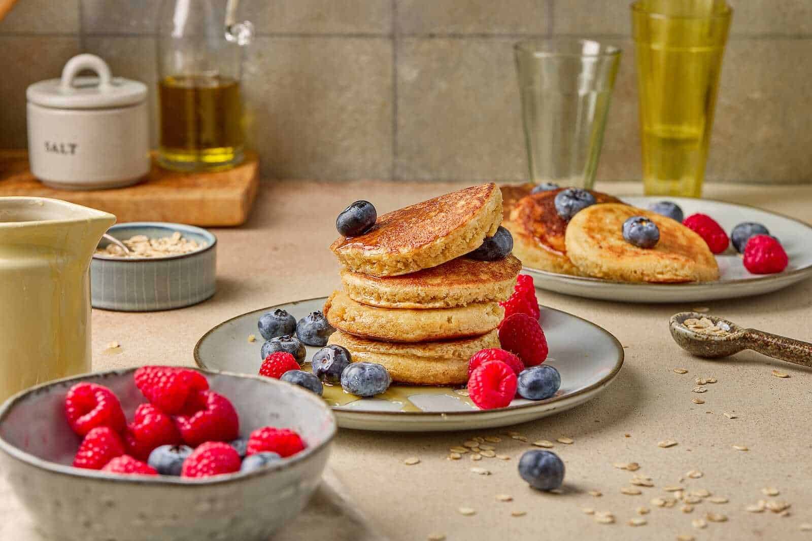 Delicious pancakes topped with blueberries and raspberries, served with fresh fruit and breakfast essentials.