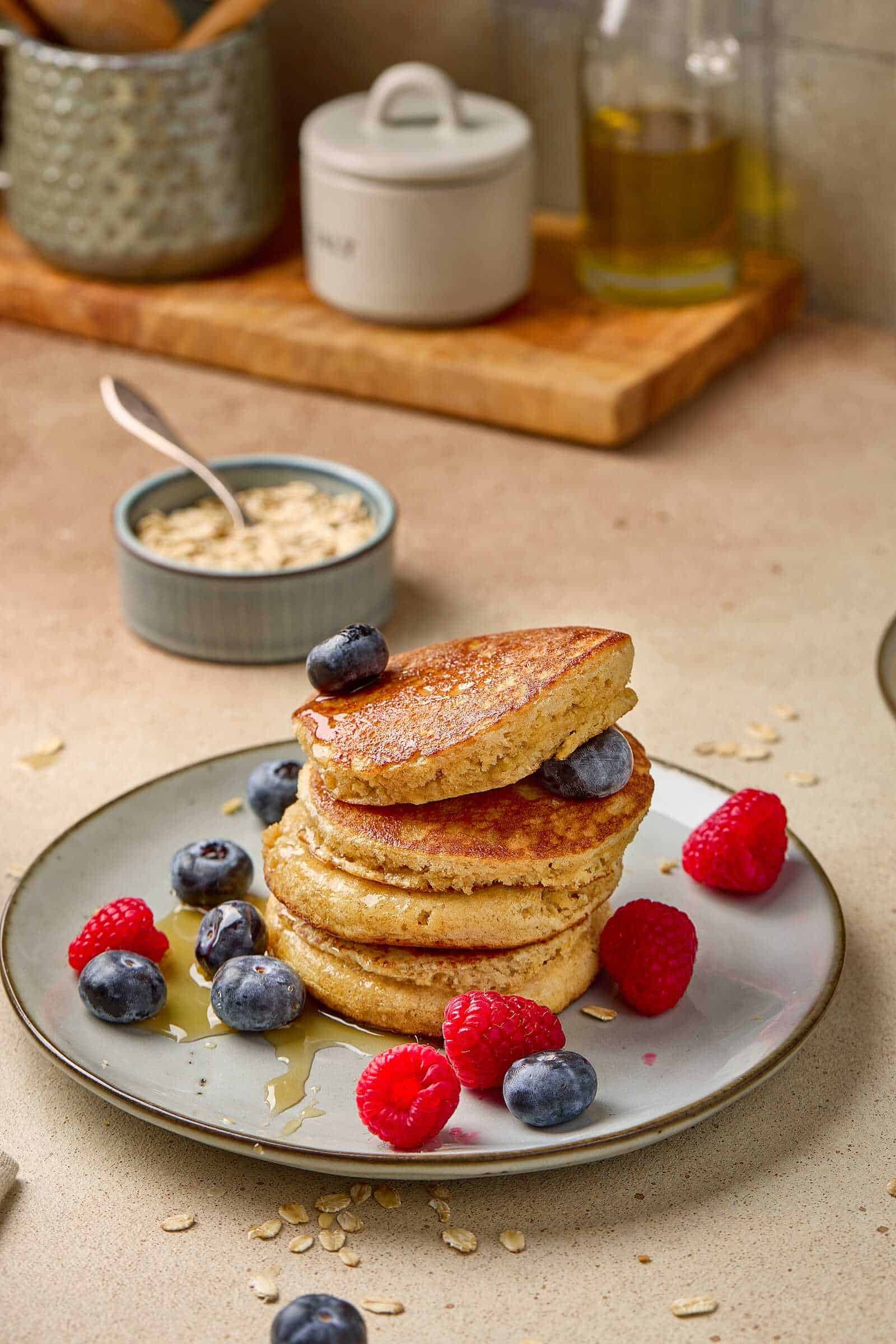 Delicious pancakes topped with blueberries and raspberries, served with syrup on a breakfast plate.