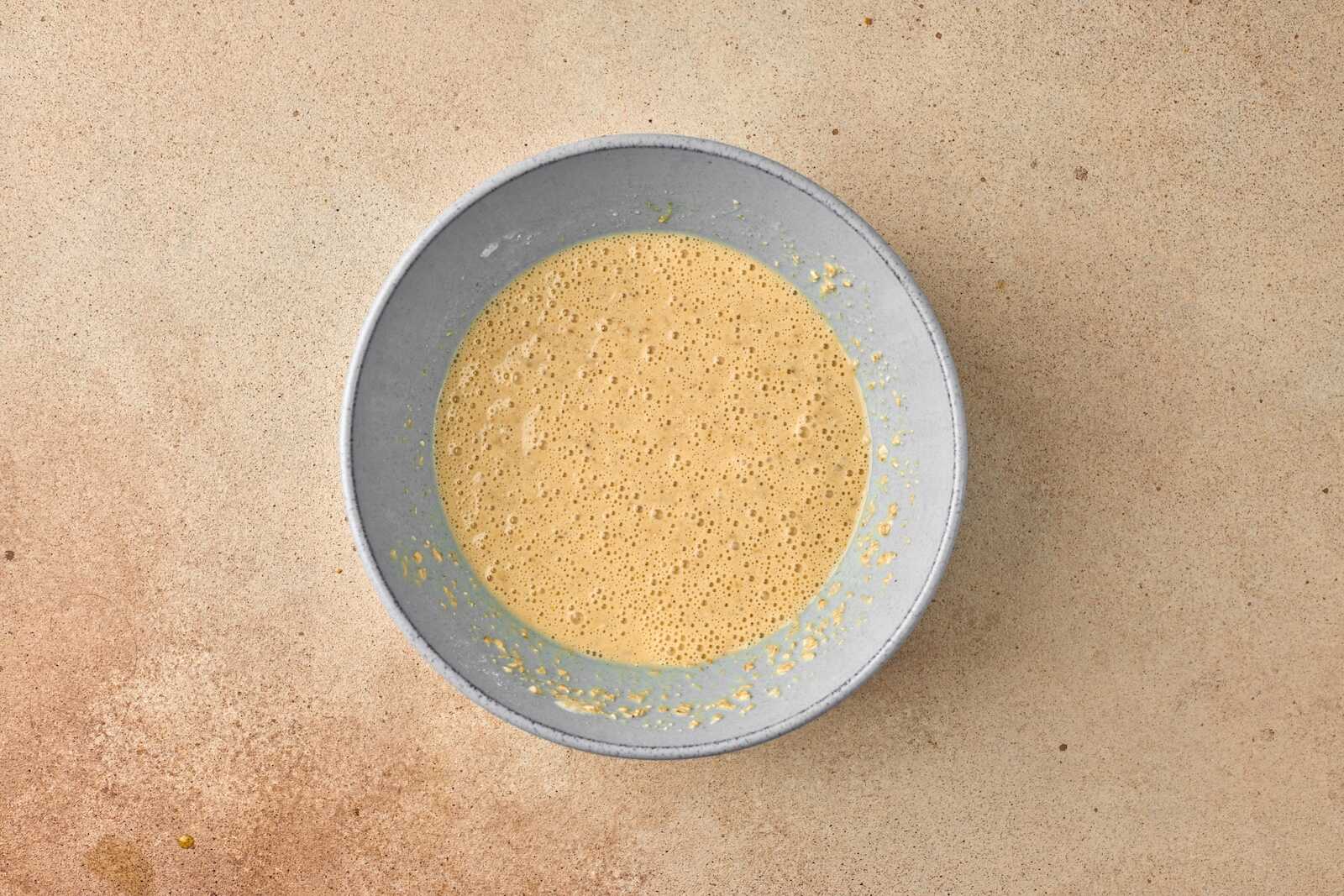 Overhead of a creamy smoothie bowl with frothy texture in a gray bowl on a beige surface, symbolizing health and wellness for surrogacy.