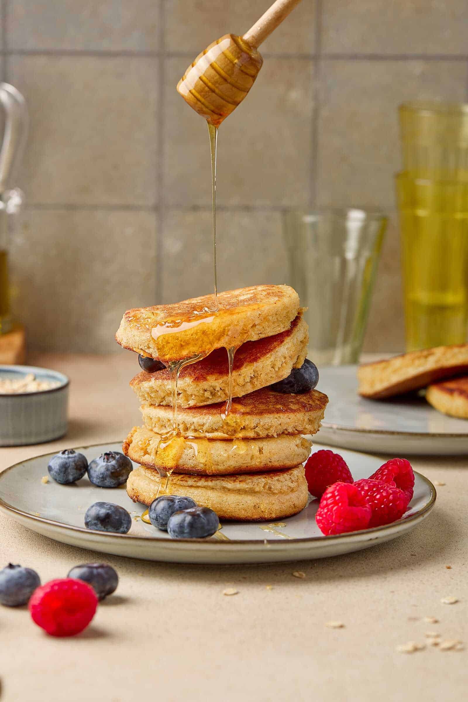 Delicious blueberry and raspberry pancakes topped with honey, fresh berries, and syrup for a perfect breakfast.