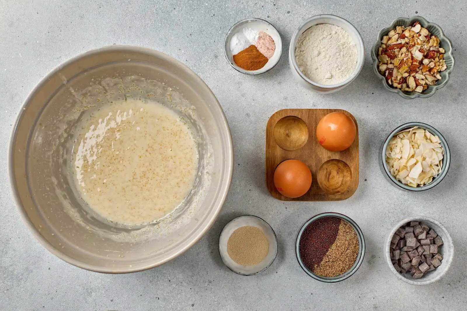 Mixing ingredients for baking with eggs, flour, chocolate, and nuts on a gray surface.