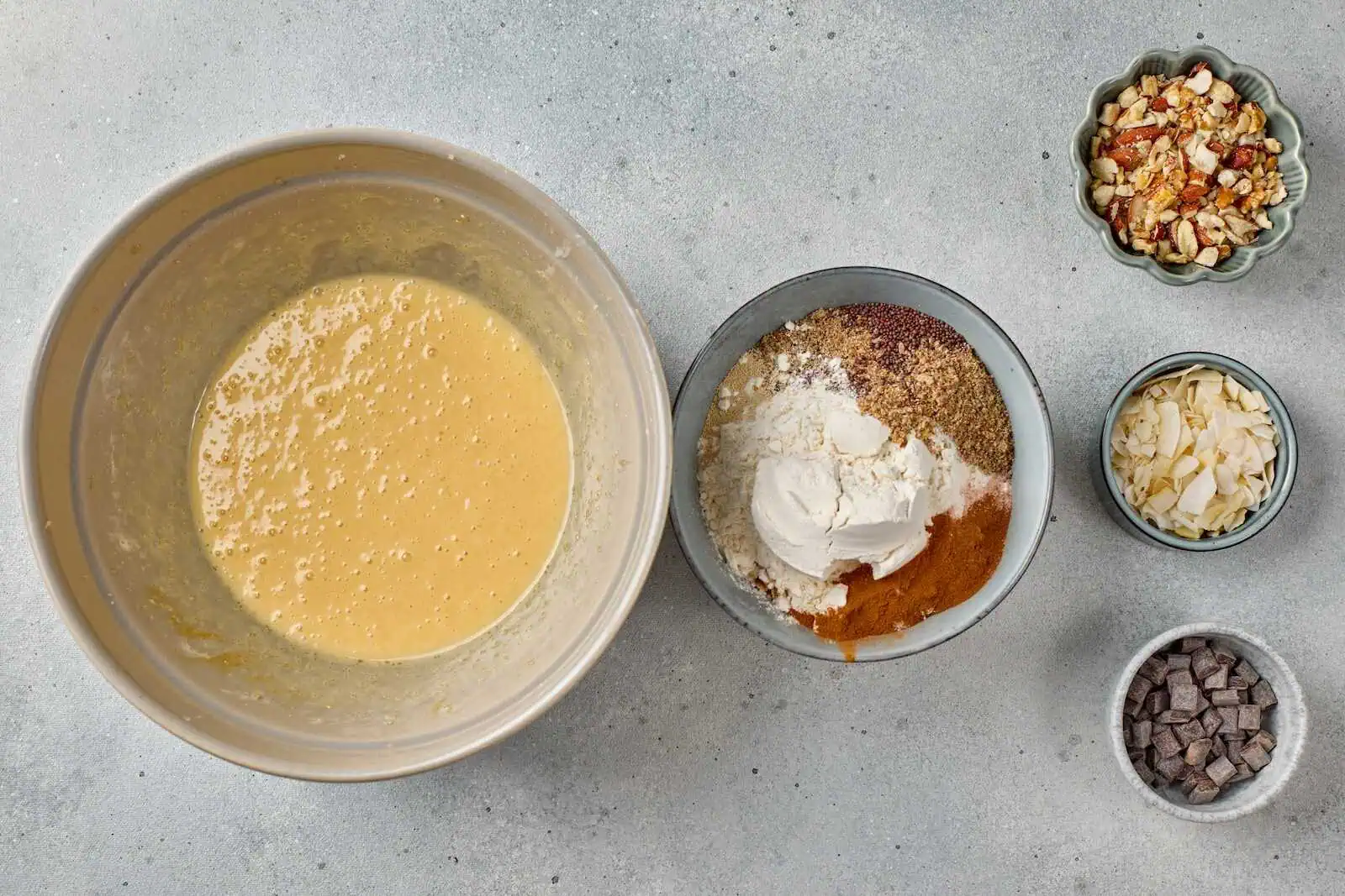 Almond, chocolate, and dried fruit ingredients for baking on a gray surface.