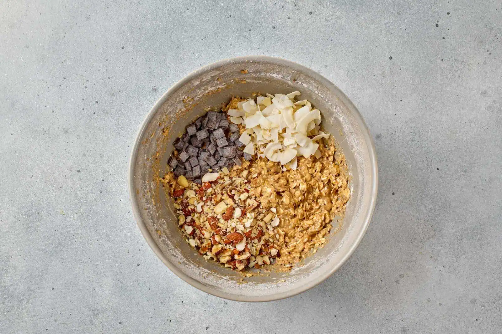 A bowl of oatmeal topped with chocolate chips, coconut flakes, chopped nuts, and dried fruits, perfect for a nutritious breakfast.