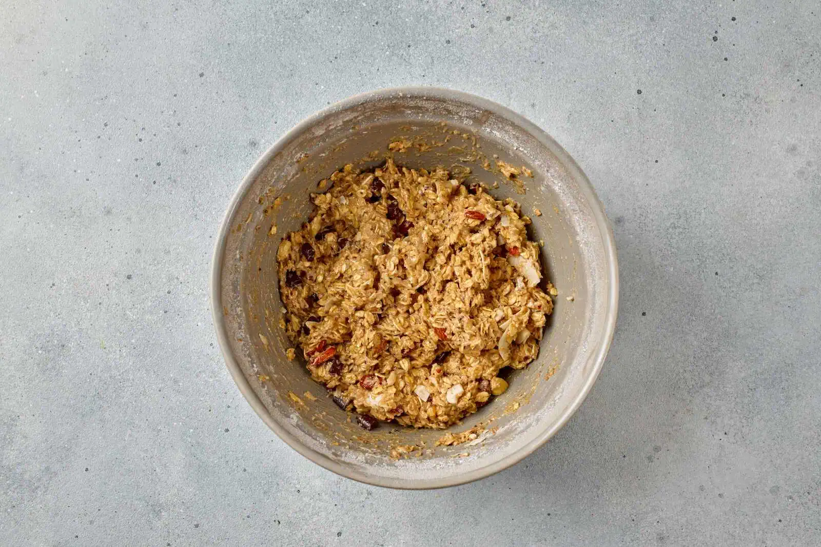 A bowl of prepared baking mixture with oats, nuts, and dried fruit for delicious baked goods.